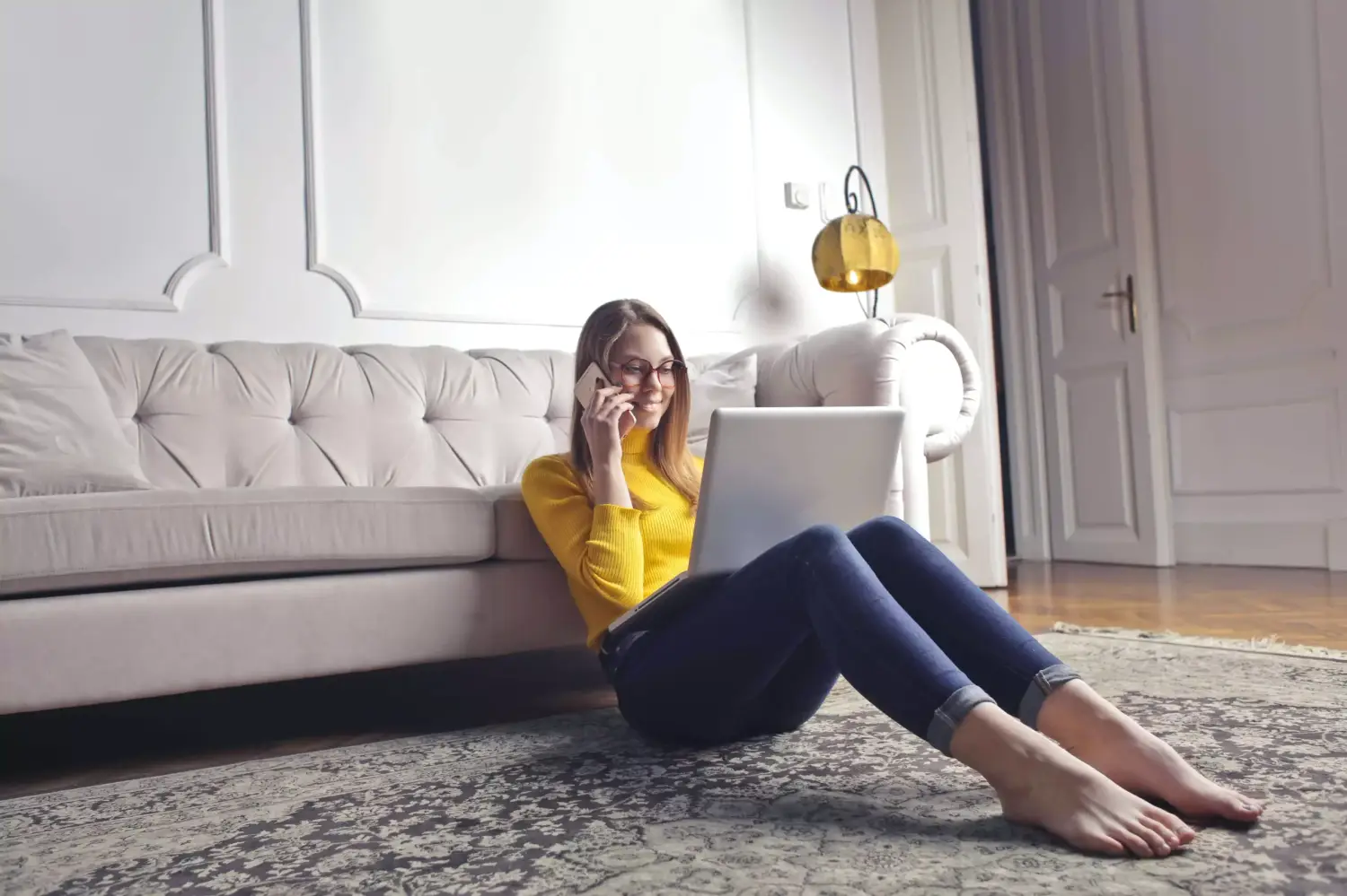 A professional woman sits on the floor of her home, working on her laptop and talking on the phone during a therapy Tampa session.