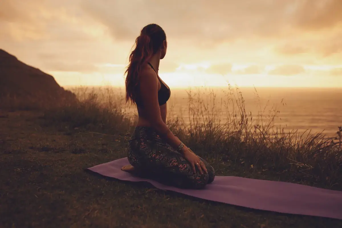 a woman kneeling on a yoag mat looking at the sunset.