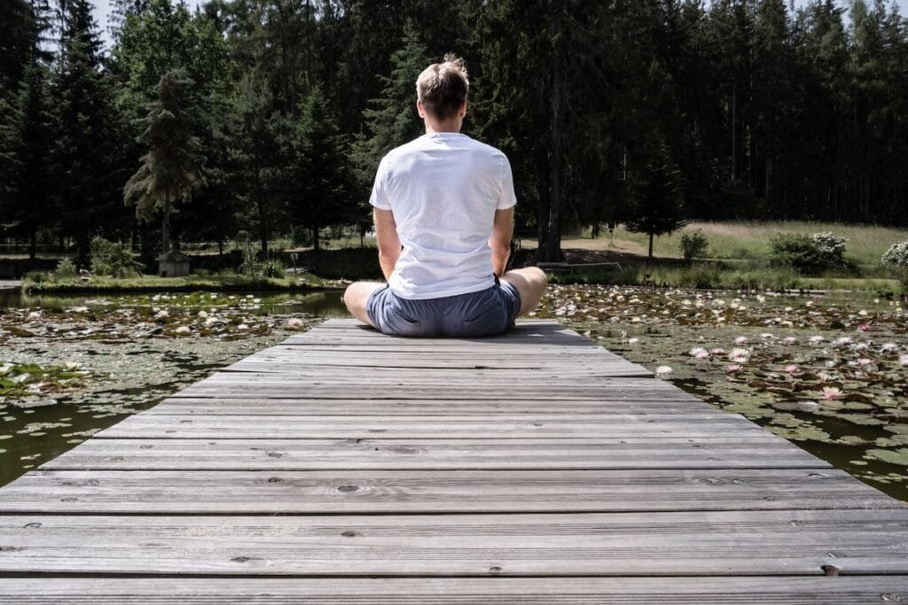 Person meditating on wooden dock by lily pond.